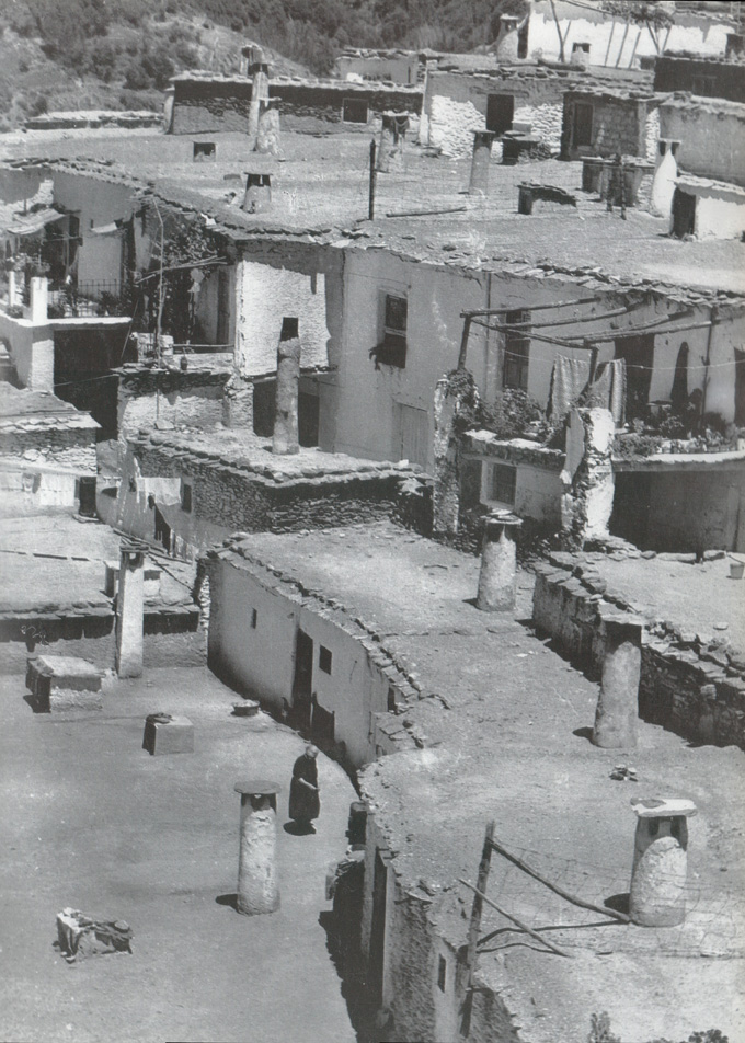 Sucesión escalonada de volúmenes cúbicos adaptados a la ladera en un pueblo de la Alpujarra, con cubiertas planas, chimeneas y tinaos
